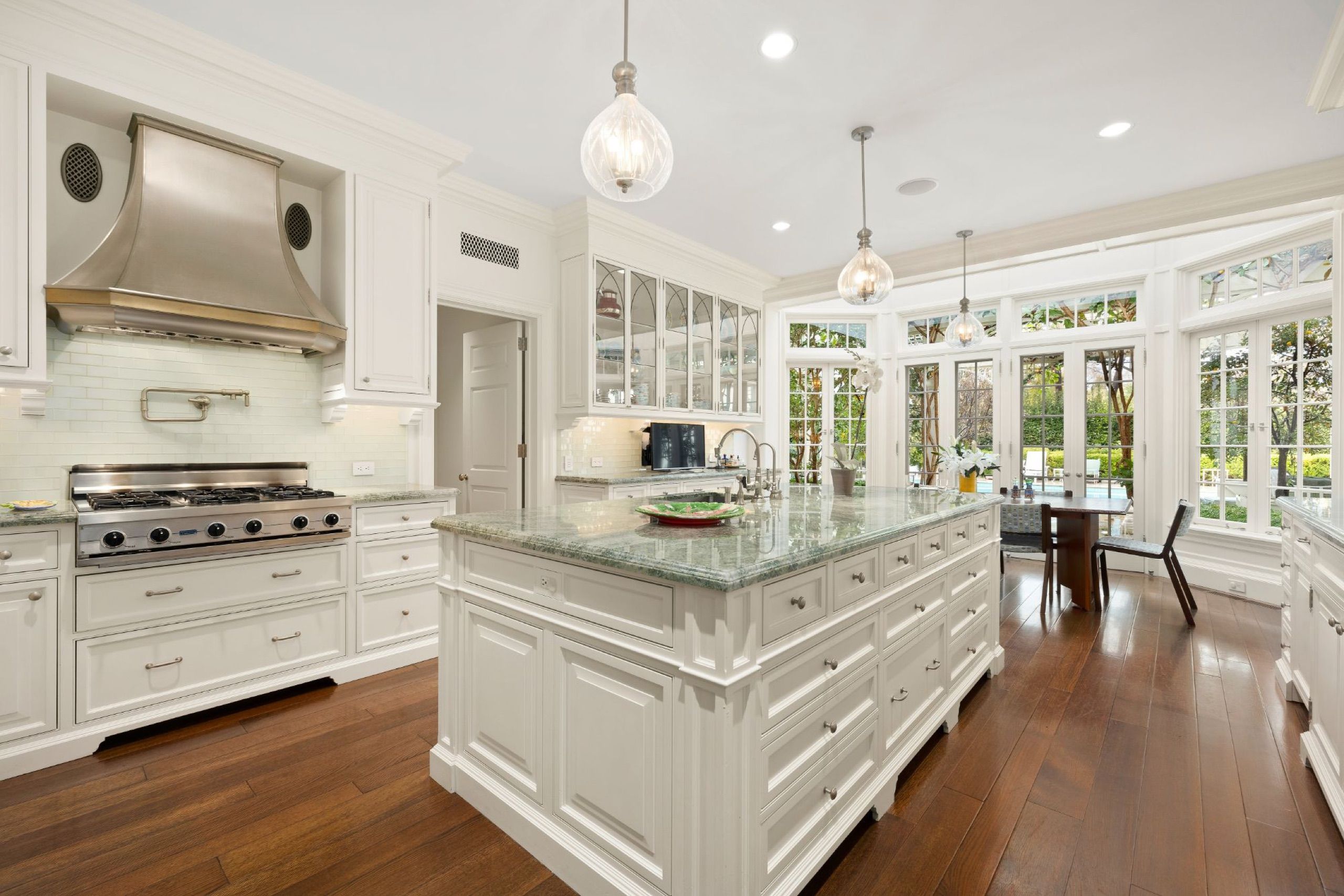 White chef's kitchen with marble island and custom steel and brass range hood