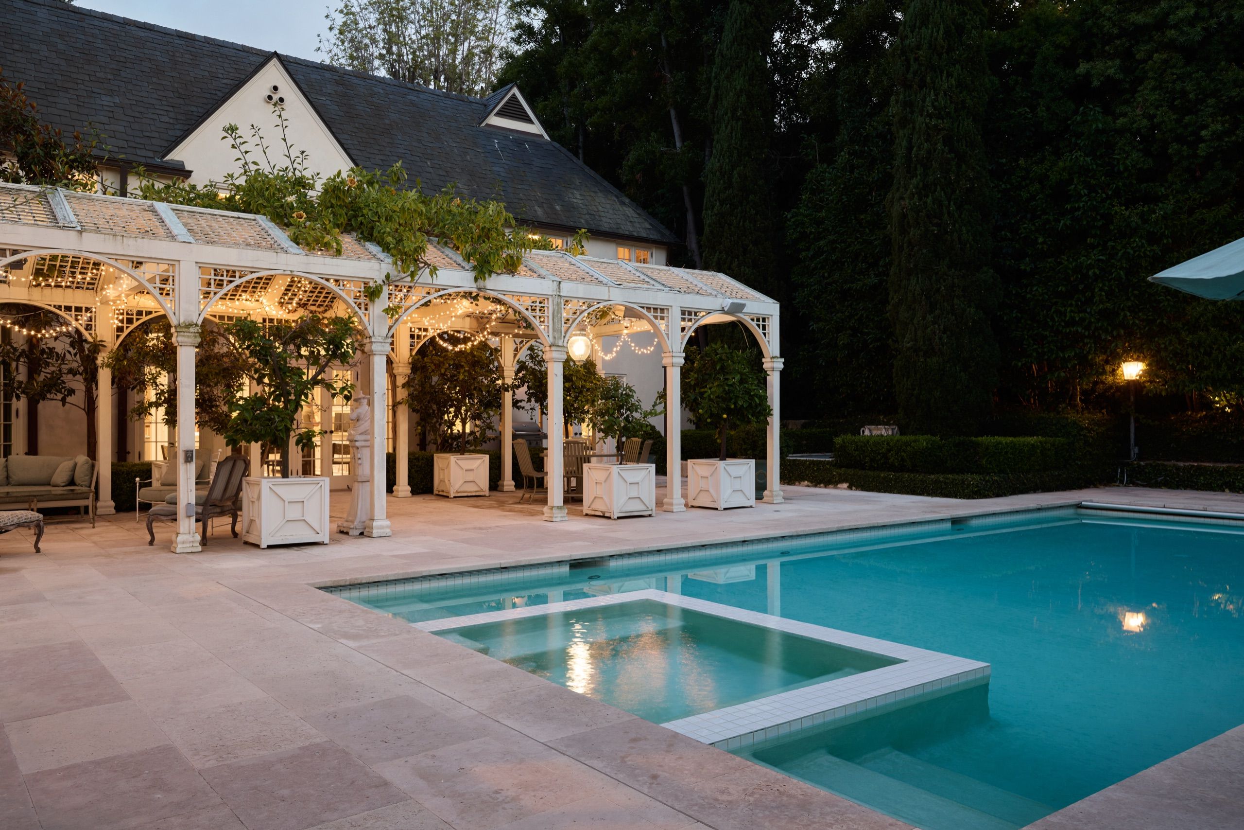 Pool, spa and pergola framed by mature trees at night